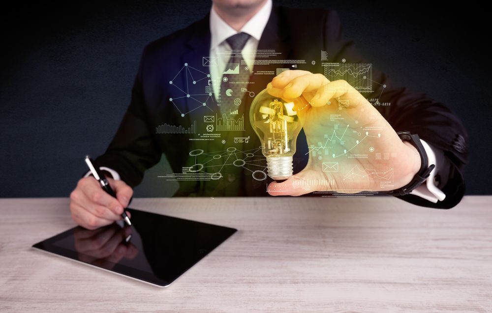 A serious business person has a complex solution concept illustrated by glowing glass light bulb in his hand with graph charts, numbers, lines, calculations.