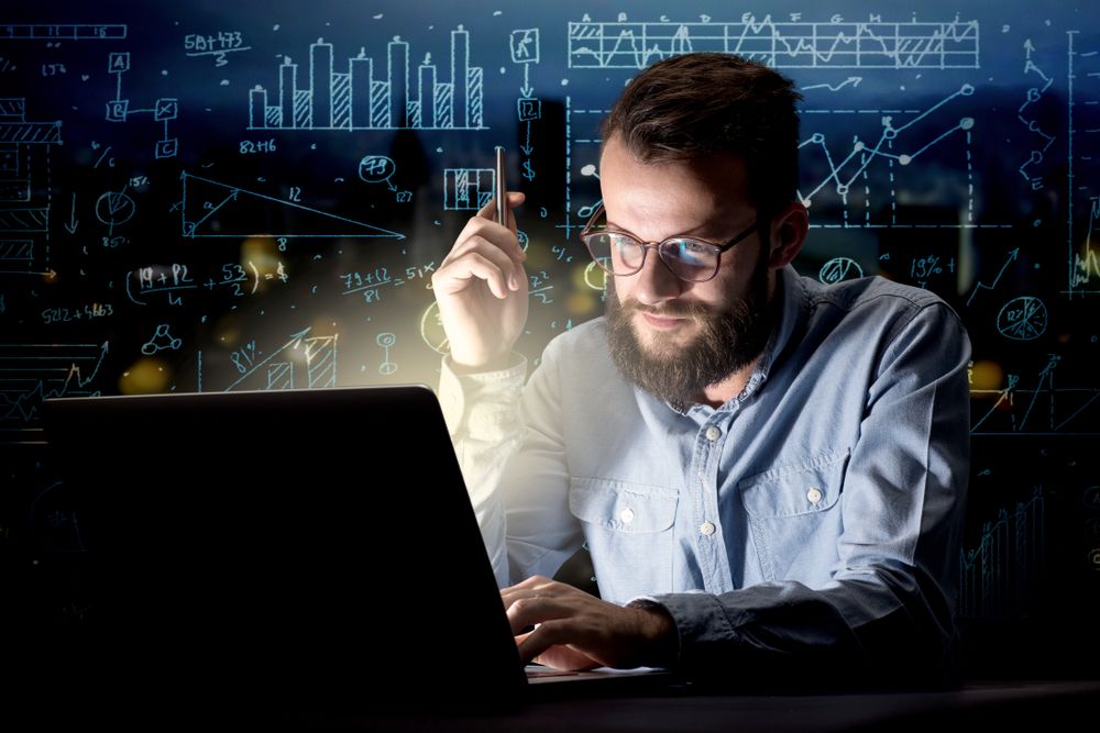 Young handsome businessman working late at night in the office with blue calculations in the background